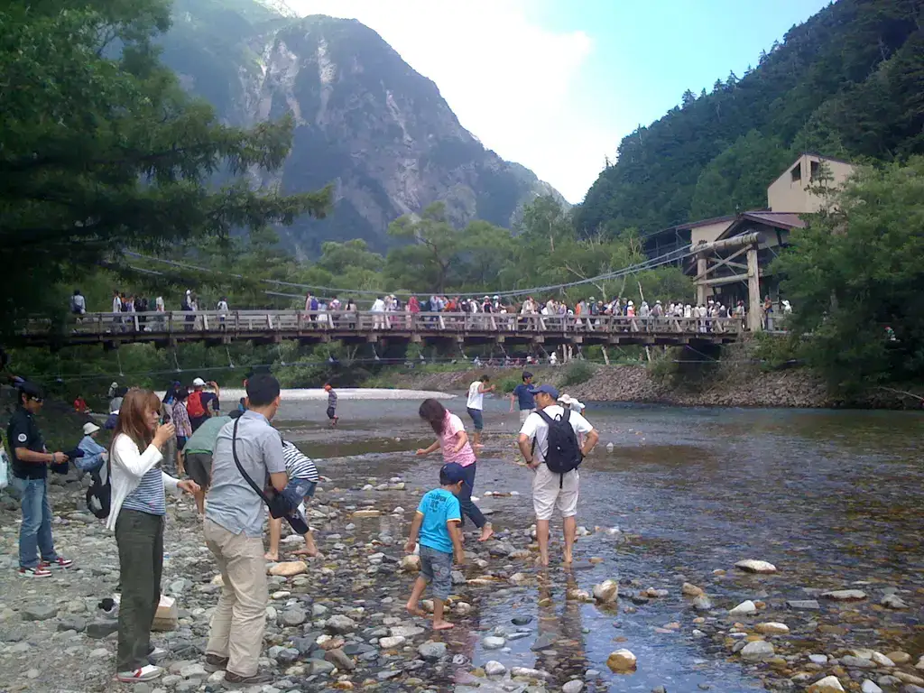 Summer visitors beside the Azusa River and Kappa Bridge with green mountain slopes behind