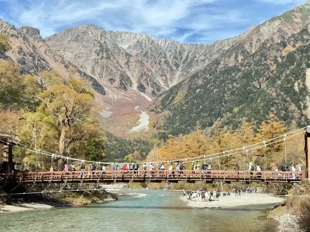 Suspension bridge over a turquoise river beneath mountain slopes