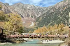 Suspension bridge over a turquoise river beneath mountain slopes
