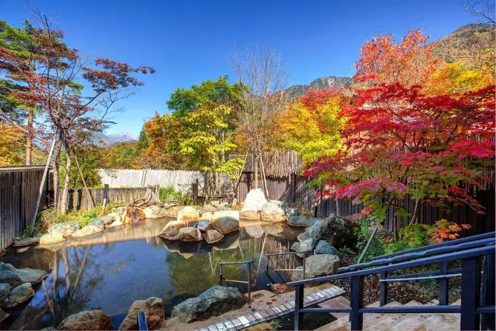 Rock-lined outdoor bath surrounded by autumn trees