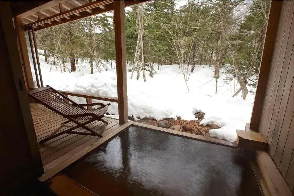 Sheltered bath beside a wooden deck overlooking snowy woodland