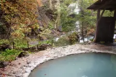 Pale blue water in a stone-edged outdoor bath at Shirahone Onsen