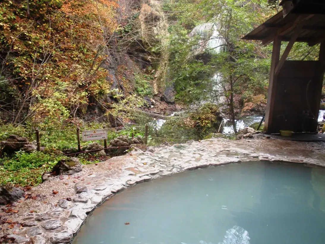 Pale blue water in a stone-edged outdoor bath at Shirahone Onsen